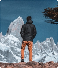 Um homem de jaqueta preta no topo de uma montanha em um ambiente aberto com clima de inverno. 