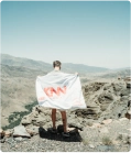 Estudante no topo de uma montanha, segurando uma bandeira branca da KNN Idiomas.